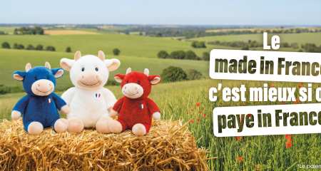 Trois vaches en peluche bleu, blanc et rouge posés sur une botte de foin